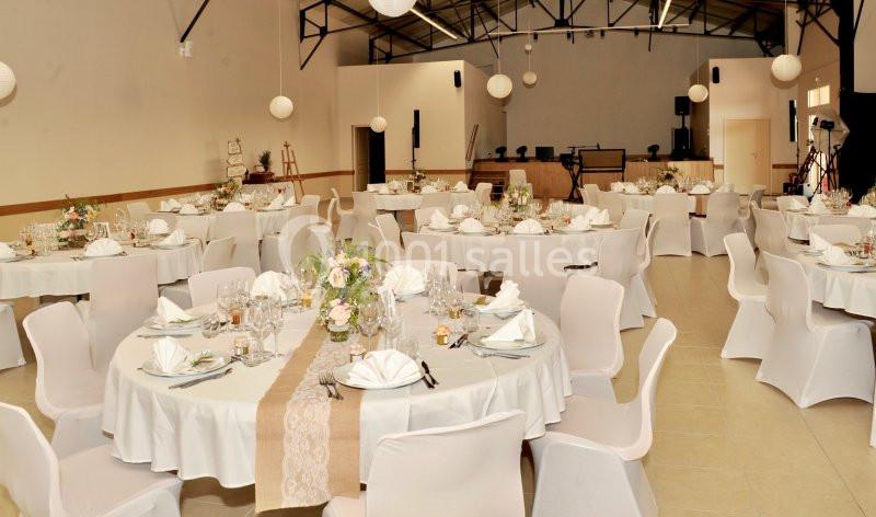 Salle de réception décorée avec des tables rondes dressées, nappes blanches, centres de table floraux et éclairage doux.