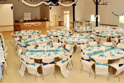 Salle avec des rangées de chaises en plastique beige face à une scène surélevée dans un espace lumineux.