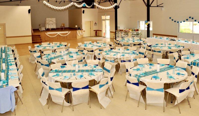 Salle de réception décorée avec des tables rondes dressées en bleu et blanc, prête pour un événement festif.