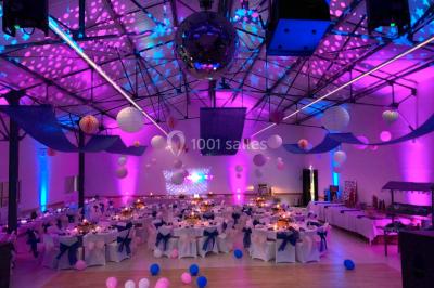 Salle avec des rangées de chaises en plastique beige face à une scène surélevée dans un espace lumineux.