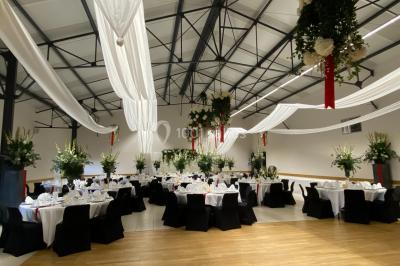 Salle avec des rangées de chaises en plastique beige face à une scène surélevée dans un espace lumineux.