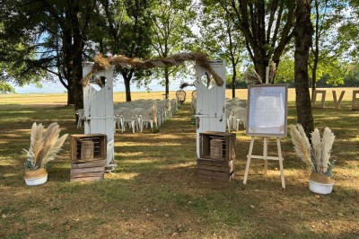 Salle avec des rangées de chaises en plastique beige face à une scène surélevée dans un espace lumineux.