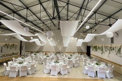 Salle avec des rangées de chaises en plastique beige face à une scène surélevée dans un espace lumineux.