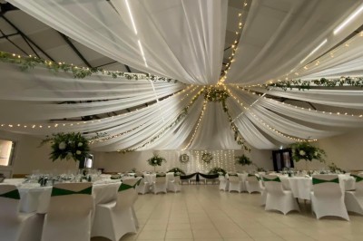 Salle avec des rangées de chaises en plastique beige face à une scène surélevée dans un espace lumineux.
