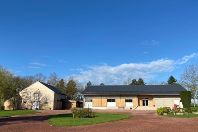 Salle avec des rangées de chaises en plastique beige face à une scène surélevée dans un espace lumineux.