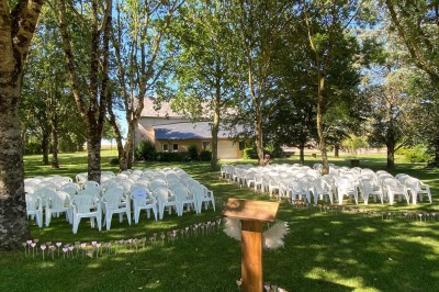 Salle avec des rangées de chaises en plastique beige face à une scène surélevée dans un espace lumineux.