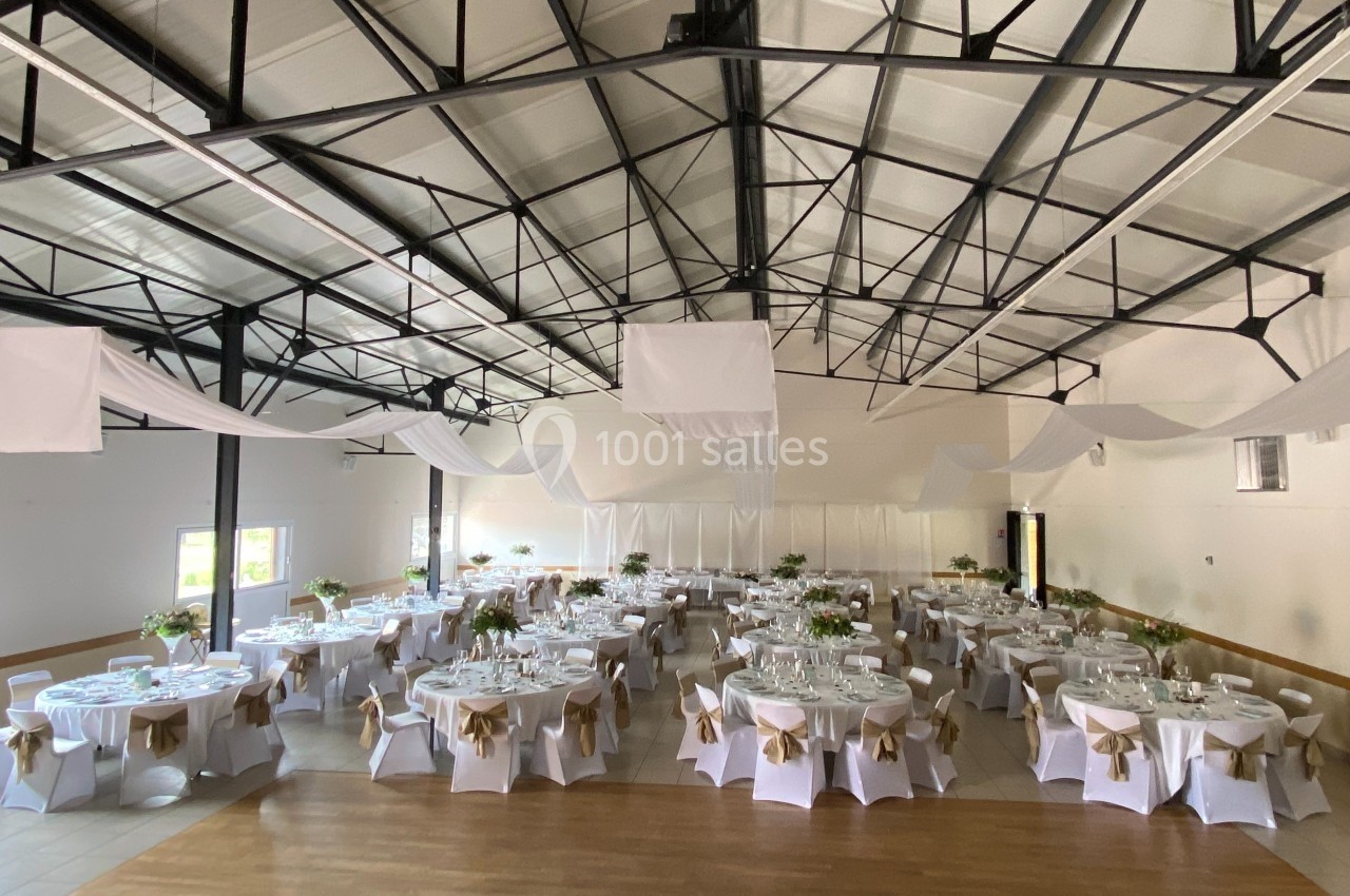 Salle de réception décorée avec des tables rondes dressées, nappes blanches et chaises ornées de nœuds beiges.