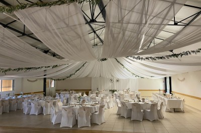 Salle avec des rangées de chaises en plastique beige face à une scène surélevée dans un espace lumineux.