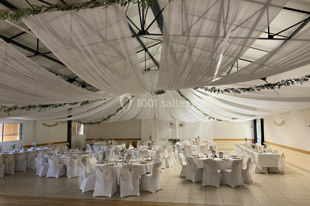 Salle de réception décorée avec des drapés blancs au plafond, tables dressées et chaises couvertes de housses blanches.