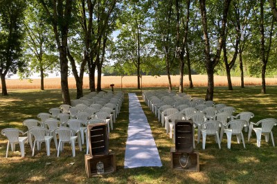 Salle avec des rangées de chaises en plastique beige face à une scène surélevée dans un espace lumineux.
