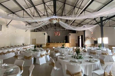 Salle avec des rangées de chaises en plastique beige face à une scène surélevée dans un espace lumineux.