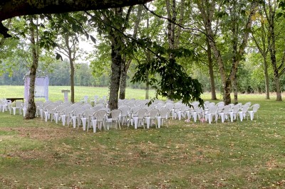 Salle avec des rangées de chaises en plastique beige face à une scène surélevée dans un espace lumineux.