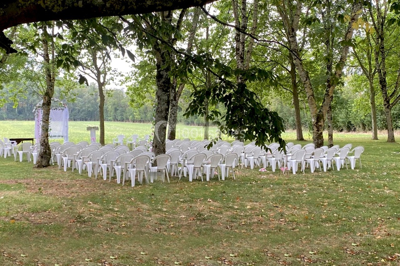 Chaises blanches disposées en extérieur sous des arbres, formant un espace pour un événement en plein air.