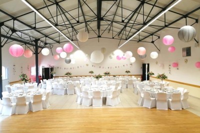 Salle avec des rangées de chaises en plastique beige face à une scène surélevée dans un espace lumineux.