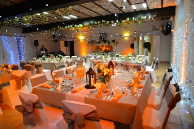 Salle avec des rangées de chaises en plastique beige face à une scène surélevée dans un espace lumineux.