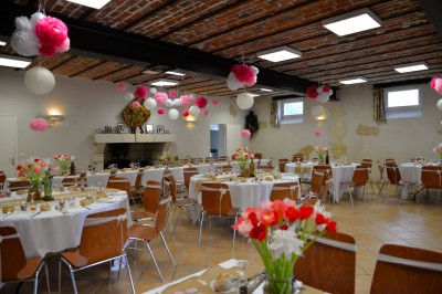 Salle avec des rangées de chaises en plastique beige face à une scène surélevée dans un espace lumineux.