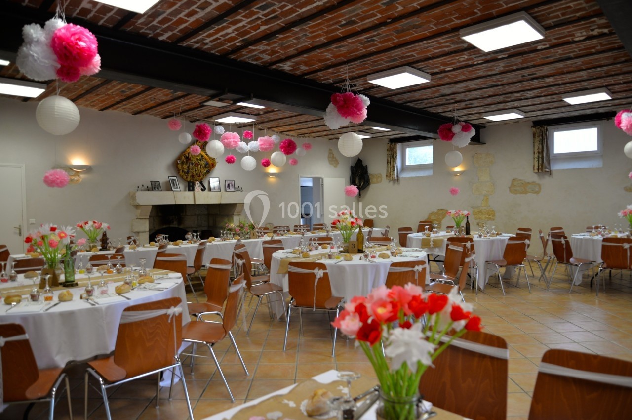 Salle de réception décorée avec des tables rondes, nappes blanches, fleurs colorées et lanternes suspendues.