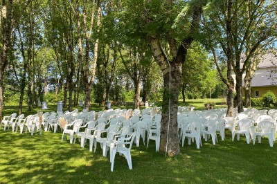 Salle avec des rangées de chaises en plastique beige face à une scène surélevée dans un espace lumineux.