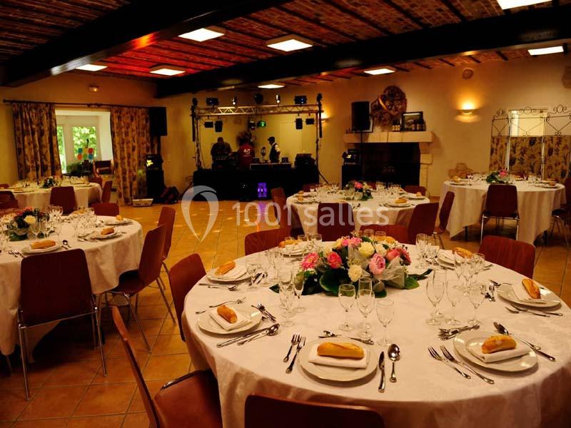 Salle de réception décorée avec des tables rondes dressées, ornées de fleurs, et une piste de danse avec équipement sonore.