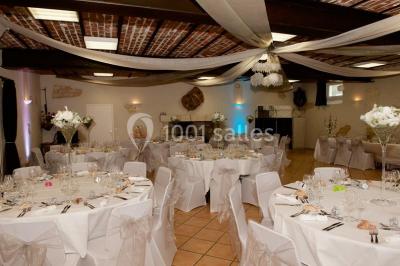 Salle avec des rangées de chaises en plastique beige face à une scène surélevée dans un espace lumineux.