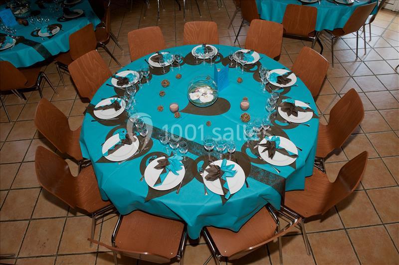 Table ronde dressée avec une nappe turquoise, des serviettes brunes, des verres et une décoration centrale élégante.