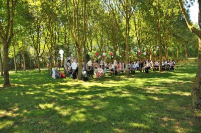 Salle avec des rangées de chaises en plastique beige face à une scène surélevée dans un espace lumineux.