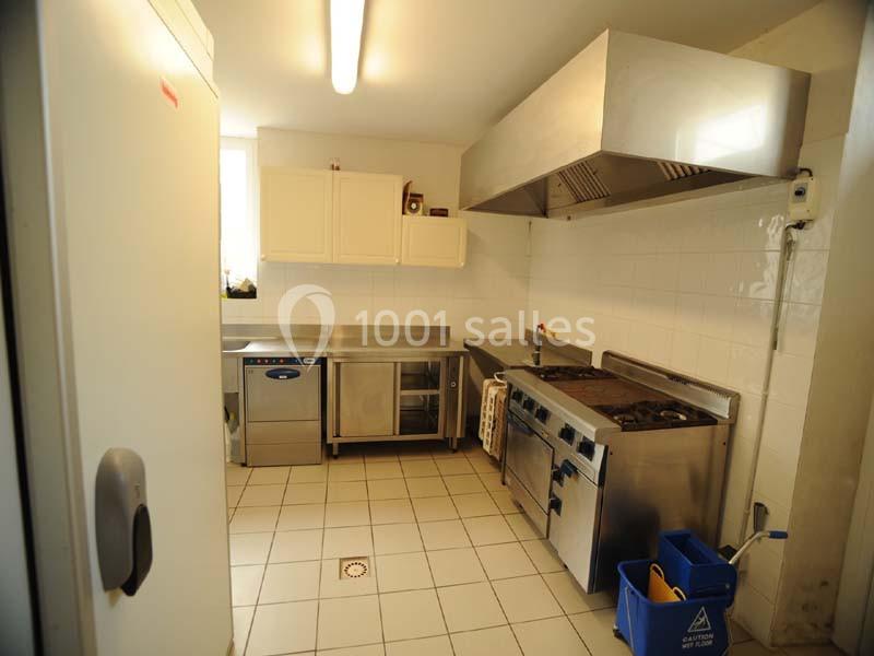 Cuisine professionnelle équipée avec plan de travail en inox, plaques de cuisson, hotte et rangements muraux.