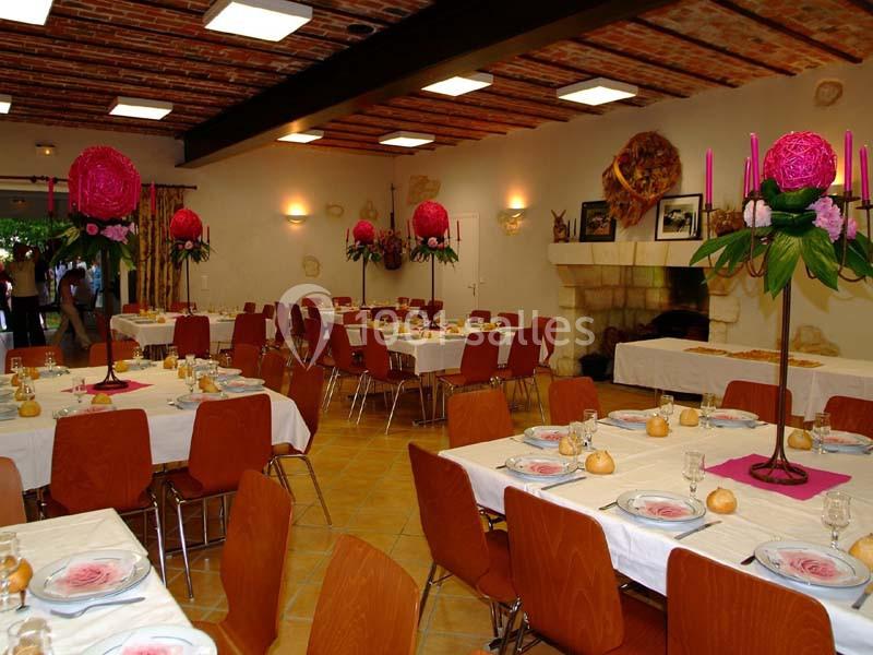 Salle de réception décorée avec des tables dressées, des chaises en bois et des centres de table fleuris roses.