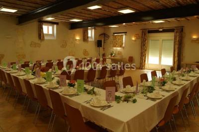 Salle avec des rangées de chaises en plastique beige face à une scène surélevée dans un espace lumineux.