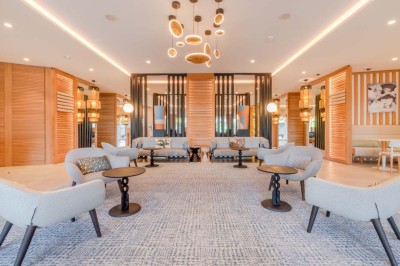 Chambre d'hôtel lumineuse avec lit double, bureau, fauteuil, grandes fenêtres et vue sur un balcon.