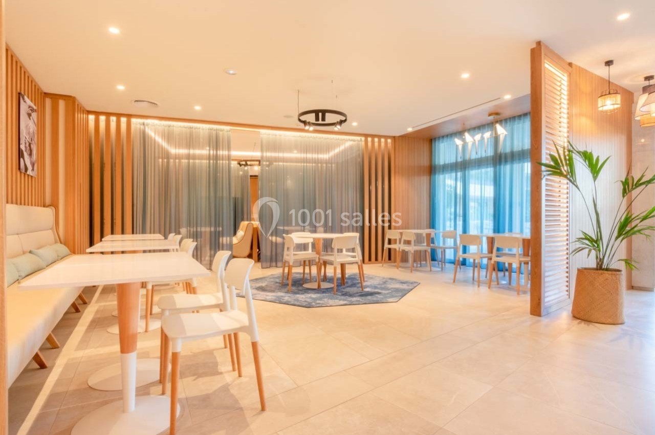 Salle lumineuse avec tables et chaises modernes, décorée de bois clair, rideaux bleus et plantes en pot.