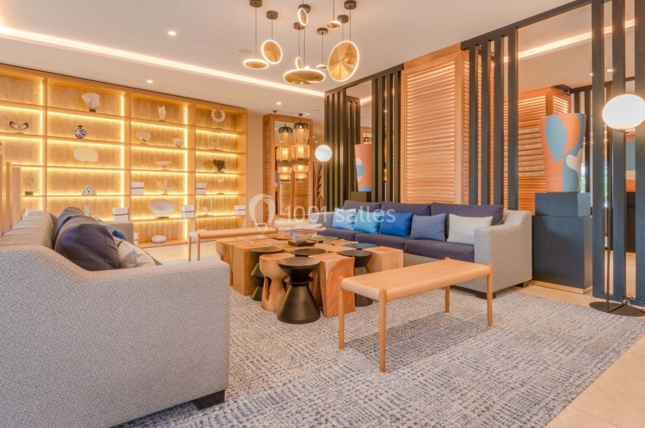 Salon moderne avec canapés, tables en bois, étagères éclairées et luminaires suspendus dans un décor chaleureux.