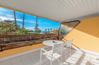 Chambre d'hôtel lumineuse avec lit double, bureau, fauteuil, grandes fenêtres et vue sur un balcon.