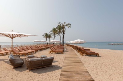 Chambre d'hôtel lumineuse avec lit double, bureau, fauteuil, grandes fenêtres et vue sur un balcon.