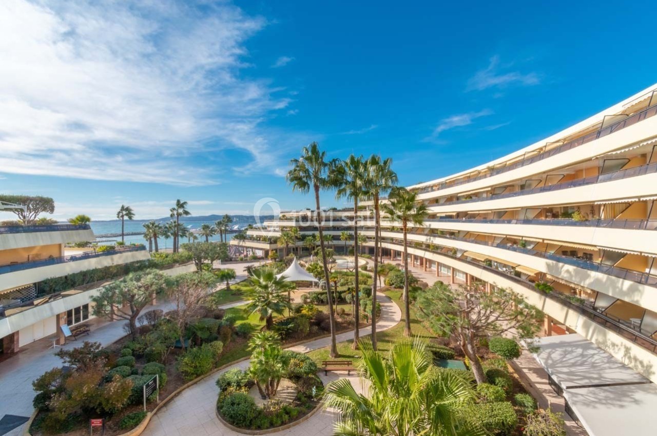 Vue d'une cour intérieure avec jardin paysager, entourée de bâtiments modernes en arc, sous un ciel bleu dégagé.