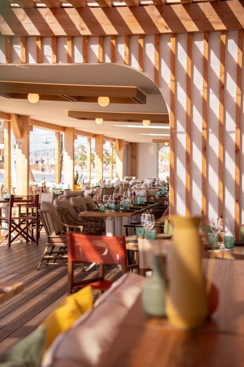 Terrasse d'un restaurant avec mobilier en bois, tables dressées et lumière naturelle filtrée par une pergola.