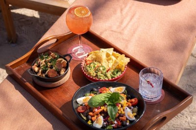 Chambre d'hôtel lumineuse avec lit double, bureau, fauteuil, grandes fenêtres et vue sur un balcon.