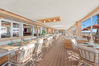 Balcon avec table et chaises blanches, vue sur des palmiers, la mer et un ciel bleu, sous un toit en panneaux blancs.