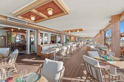 Balcon avec table et chaises blanches, vue sur des palmiers, la mer et un ciel bleu, sous un toit en panneaux blancs.