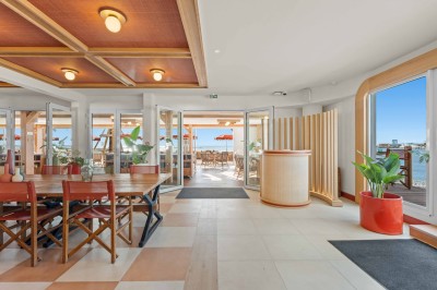 Balcon avec table et chaises blanches, vue sur des palmiers, la mer et un ciel bleu, sous un toit en panneaux blancs.