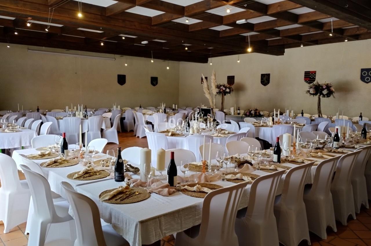 Salle de réception décorée avec des tables dressées, nappes blanches, chandeliers et chaises blanches alignées.