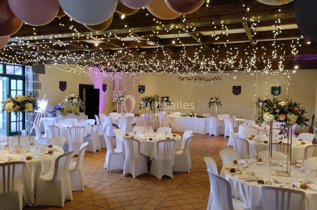 Salle de réception décorée pour un mariage, avec tables dressées, guirlandes lumineuses et ballons suspendus.