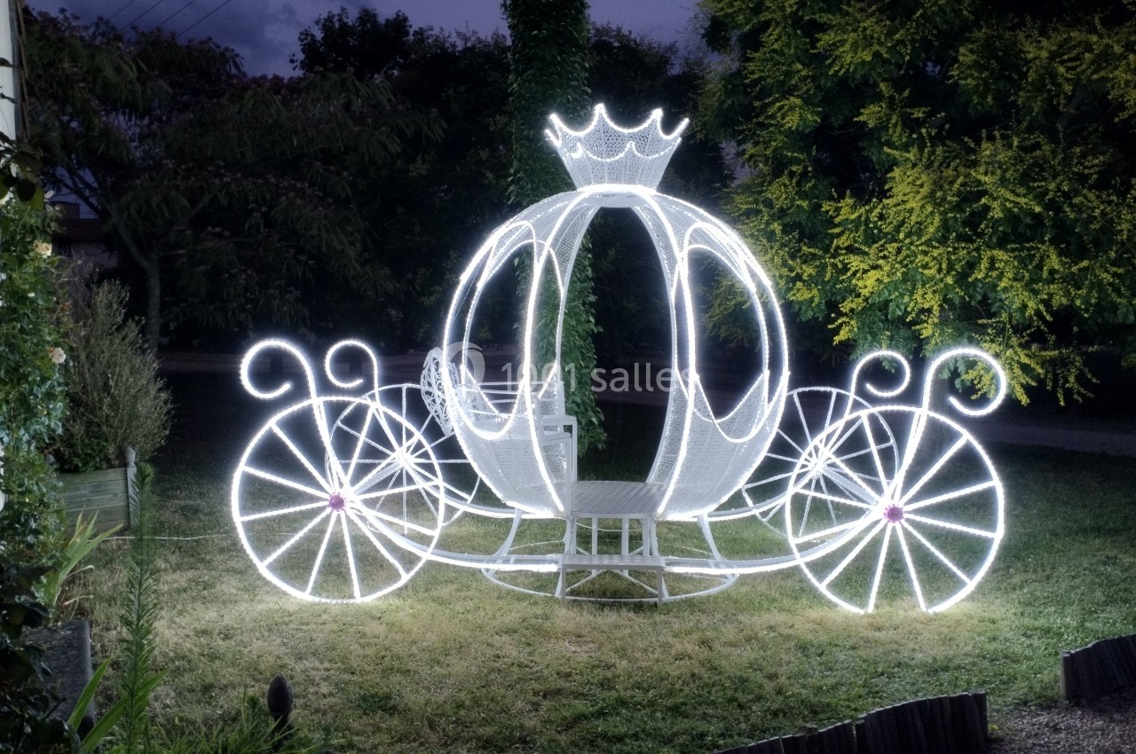 Carrosse lumineux en forme de citrouille avec une couronne, installé dans un jardin en soirée.