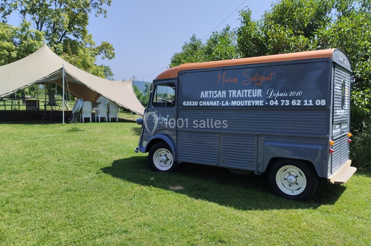 Camion gris d'un artisan traiteur stationné sur une pelouse près d'une tente beige en plein air.
