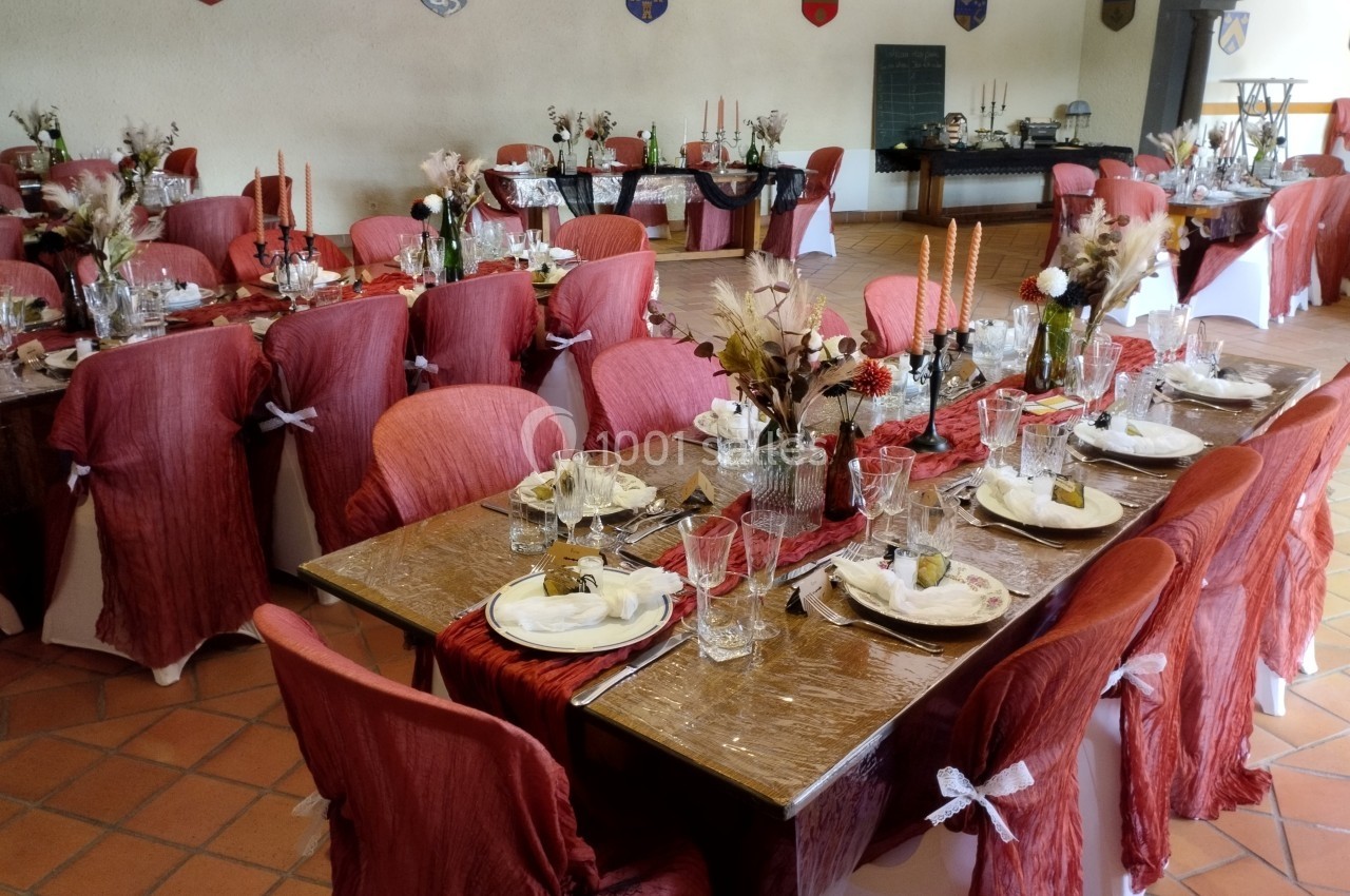Salle de réception décorée pour un événement, avec tables dressées, nappes rouges et éléments floraux.