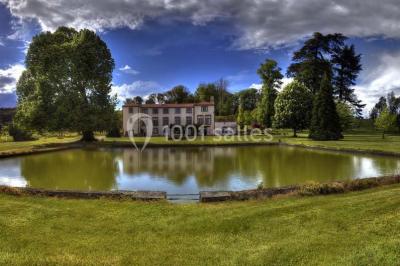 Étang naturel entouré de végétation, avec des chaises longues en arrière-plan et des pierres au premier plan.