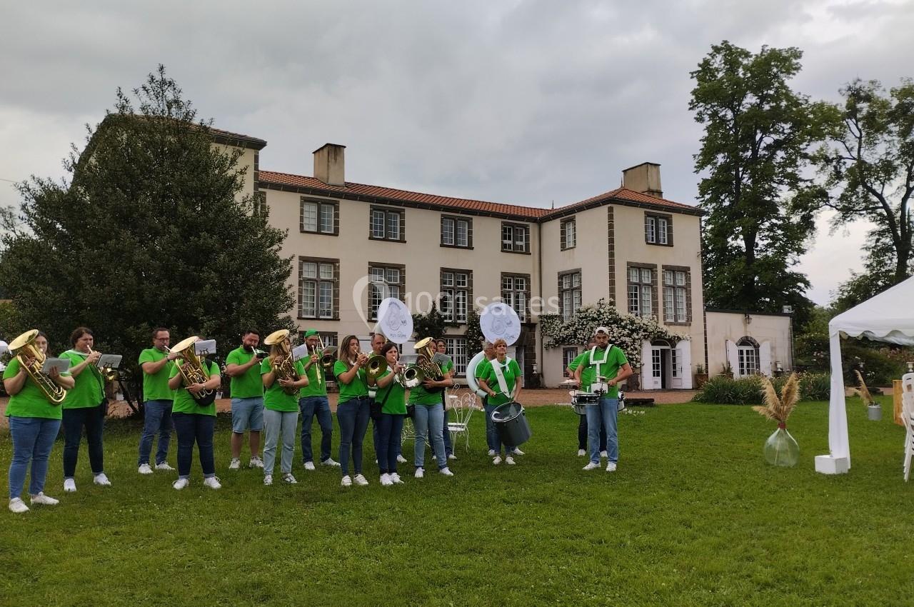 Un groupe de musiciens en tenue verte joue des instruments devant un grand bâtiment entouré de verdure.