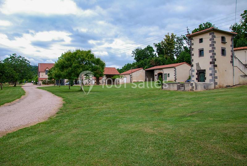 Chemin de gravier menant à un ensemble de bâtiments avec toits en tuiles, entourés de pelouses et d'arbres.