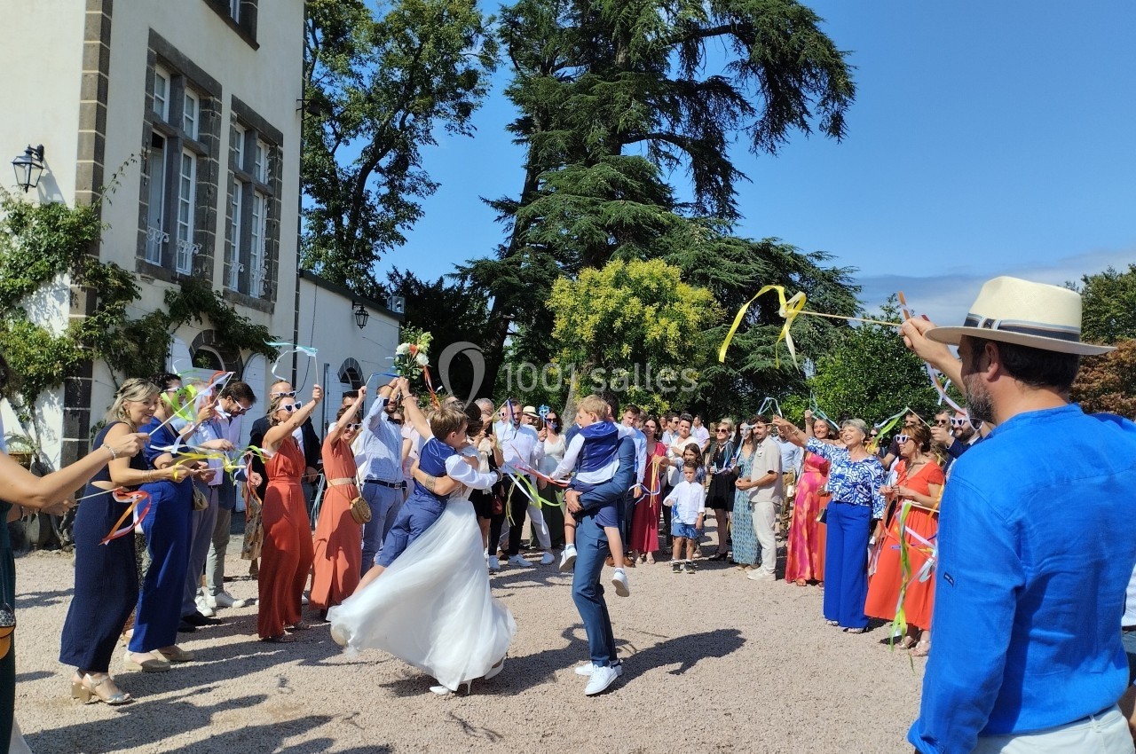 Un couple de mariés traverse une haie d'honneur festive avec des invités agitant des rubans colorés.