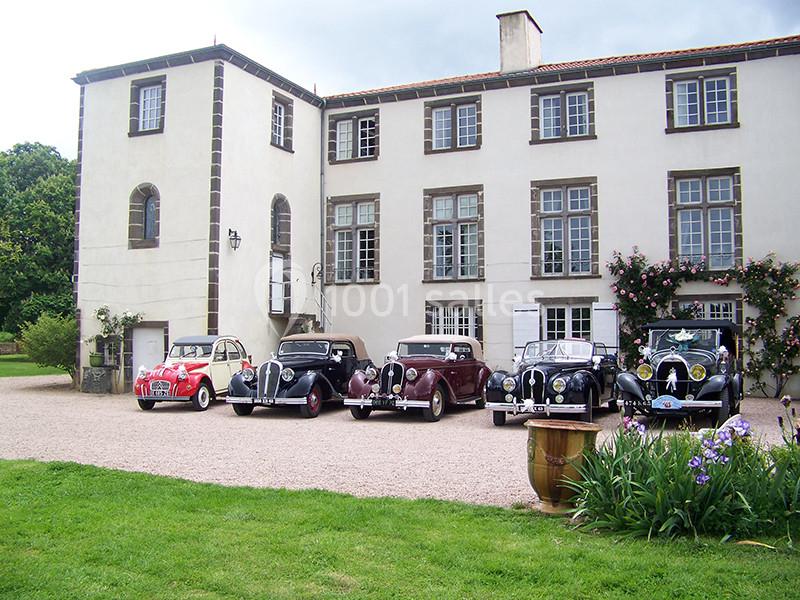 Cinq voitures anciennes alignées devant une grande maison de style traditionnel avec jardin et allée gravillonnée.